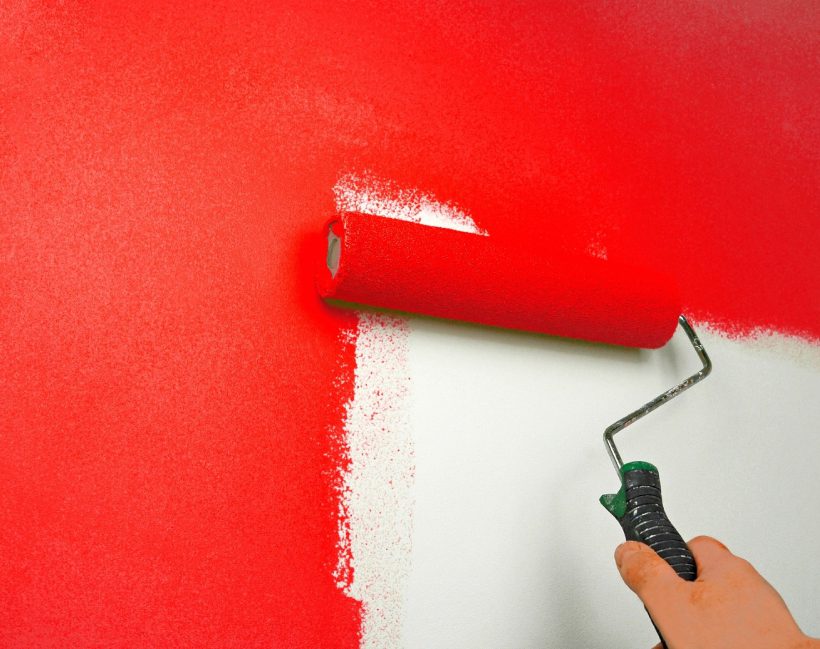 A person painting the wall red with paint roller.