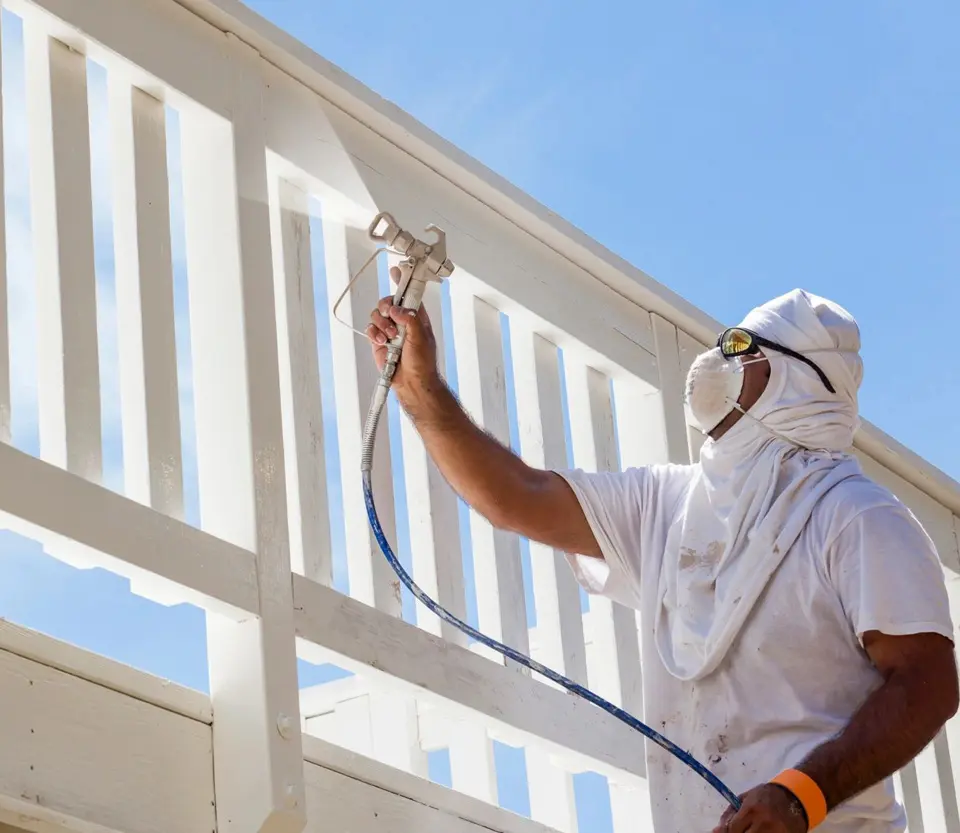 A man in white shirt painting wooden structure.
